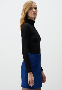 Schwarzer Rollkragenpullover kombiniert mit einem strukturierten, hellblauen Miniröckchen. Das Outfit weist eine körpernahe Silhouette und eine glatte Oberfläche auf.