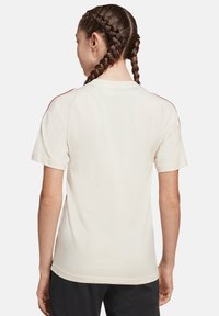 T-shirt blanc à manches courtes avec des accents rouges le long des épaules, doté d'un col rond et d'une coupe décontractée. Texture en coton lisse.