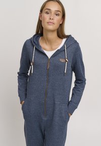 Navy blå zip-up jumpsuit laget av mykt stoff med hette, med logo-patch, dekorative snorer og sidelommer.