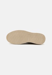 Suela de goma beige con un patrón texturizado, que presenta ranuras horizontales y verticales para agarre. Diseño plano con un borde circular.