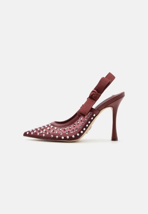 Bordeauxfarbene Slingback-Pumps mit spitzer Spitze, silbernen Nieten und einem strukturierten Schleifenriemen vor weißem Hintergrund.