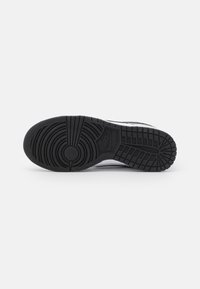 Black rubber sneaker sole with circular and linear tread patterns, featuring a raised Nike logo. Textured surface for grip and durability.