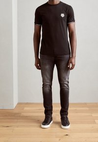 Camiseta negra de manga corta con un pequeño logo en el pecho, combinada con jeans oscuros y zapatillas negras con suelas blancas.