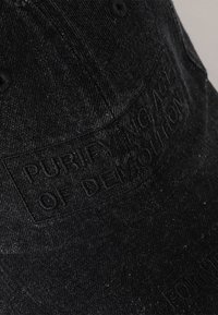 Black denim cap featuring raised text "PURIFYING ACT OF DEMOLITION" on the front, with a structured shape and subtle texture.