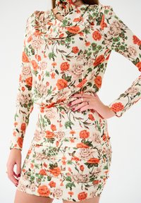 Sukienka w kwiatowy wzór z długimi rękawami, drapowanym dekoltem i marszczeniem w jasnym kremowym, pomarańczowym i zielonym kolorze.