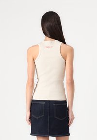 Beige geribbelde tanktop met een ronde halslijn en een rood "REPLAY" logo op de achterkant, gecombineerd met een donkere denimrok met dubbele achterzakken.