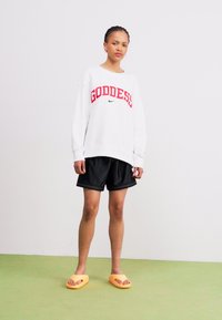White sweatshirt with red "GODDESS" text and Nike logo, paired with black shorts and orange slide sandals. Simple design, casual outfit.