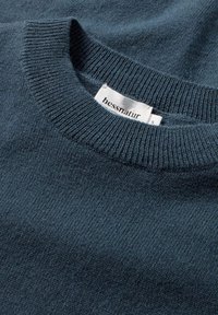 Marineblauwe gebreide trui met een geribde ronde hals. Het materiaal lijkt zacht en gestructureerd. Etiket zichtbaar met het merk "hessnatur" en maat "S."