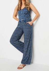 Džínový overal s přiléhavým topem, dvěma předními kapsami a širokými kalhotami se vzorem v tmavě modré barvě se bílými květinovými akcenty.