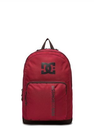Rød DC Shoes rygsæk med sort logo øverst og frontlynlåslomme med lodret "DCSHOECOUSA" tekst.