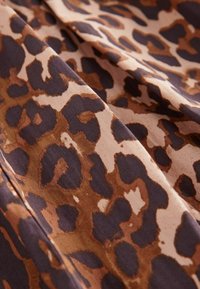 Jednoduchá látka s leopardím potiskem v odstínech hnědé a černé na světlém béžovém pozadí, s hladkou strukturou a volnými záhyby.