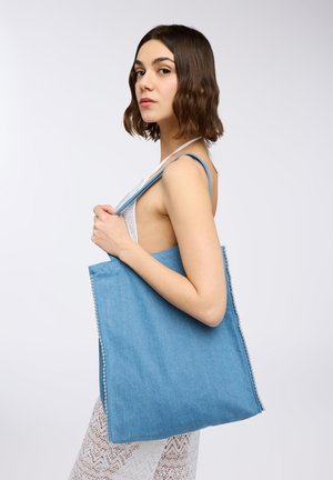Borsa tote in denim di colore blu chiaro con dettagli di perline sui lati. La borsa ha manici robusti e un design semplice e spazioso.