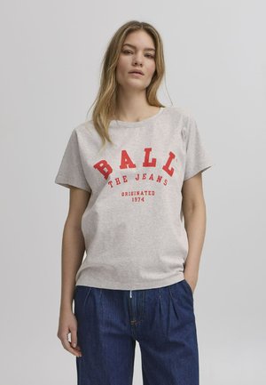 Pelēks kokvilnas T-krekls ar īsām piedurknēm, kuru rotā drosmīgs sarkans uzraksts: "BALL THE JEANS" un "ORIGINATED 1974." Apvienots ar tumši ziliem džinsu biksēm.