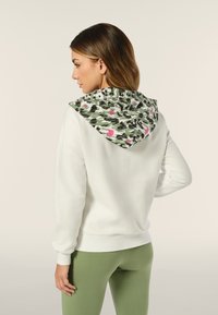 Felpa bianca con cappuccio a motivi verde e rosa, maniche lunghe e vestibilità comoda, abbinata a leggins verdi.