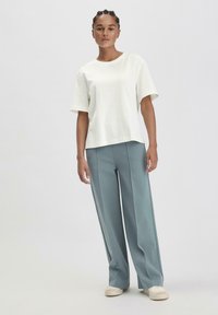 Witte katoenen T-shirt met korte mouwen, gecombineerd met lichtblauwe, wijde broek en crèmekleurige sneakers. Eenvoudige en relaxte pasvorm.