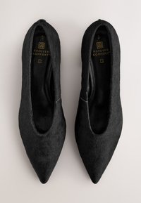 Svarta pumps i fejkpäls med spetsig tå och låg skåra på sidorna. Den inre fodringen är slät och har logotypen "Forever Comfort" präglad i guld.