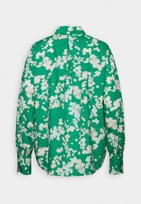 Chemise verte à manches longues avec motif floral blanc, poignets boutonnés et col, vue de dos sur un fond uni.