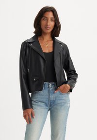 Musta keinonahasta tehty lyhyt moottoripyörätakki, jossa on viisto kaulus, vetoketjukiinnitys ja sivutaskut. Teksturoitu pinta ja hopeanväriset yksityiskohdat.