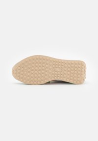 Suela de zapato con una base de goma beige, treads redondeados, logo en relieve y una textura suave para mejor tracción.