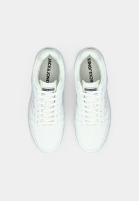 White sneakers made of smooth leather, featuring a rounded toe, lace-up design, padded collar, perforated details, and branding on the tongue.