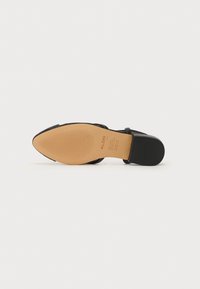 Chaussure noire à talon avec un bout pointu, présentant un dessus lisse et une semelle en caoutchouc texturée. Comprend un logo sur la semelle intérieure.