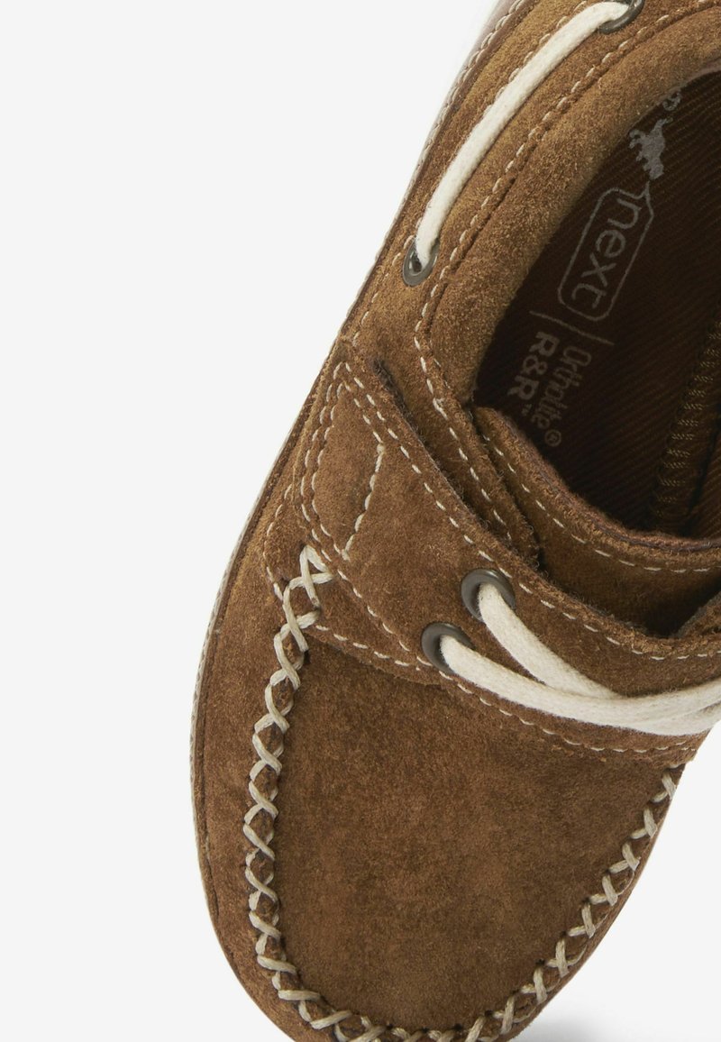 Chaussure en daim marron avec des lacets blancs, présentant des accents brodés le long du bord et une semelle intérieure texturée. Design à bout rond.