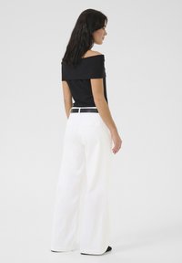 Zwarte off-shoulder top, gecombineerd met witte wijde broek en een zwarte riem. Zachte stof met een getailleerd ontwerp, dat een strakke silhouette laat zien.