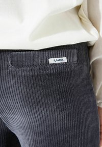 Grijze korduroy broek met verticale ribbels, een elastische tailleband en een label met de tekst "GARCIA" op de achterzak.