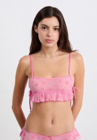 Top court en organza rose avec un motif floral, ourlet volanté et bretelles spaghetti ajustables. Tissu doux avec des accents texturés.