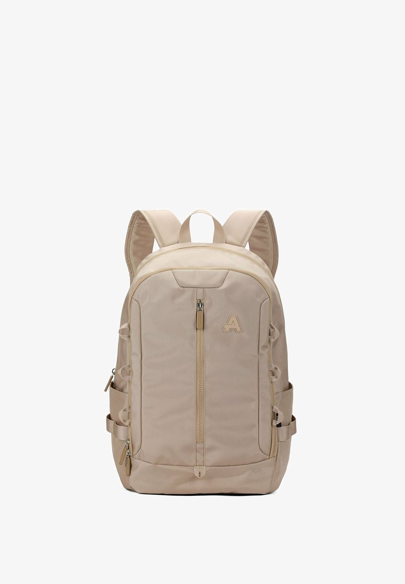 Beige stoffen rugzak met een ritssluiting hoofdvak, zijvakken, verstelbare schouderbanden en een opvallend logo aan de voorkant.