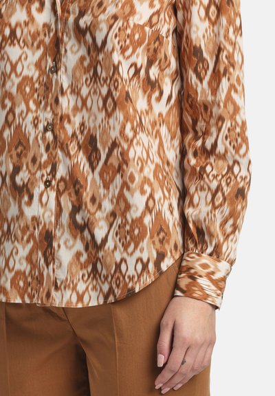 Camicia a maniche lunghe con motivo nei toni del marrone e crema, texture liscia, con bottoni e taschino sul petto.