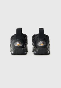Chaussures de sport noires avec une tige en mesh texturé, un col rembourré, une semelle en caoutchouc et un logo circulaire avec un motif en grille sur le talon.