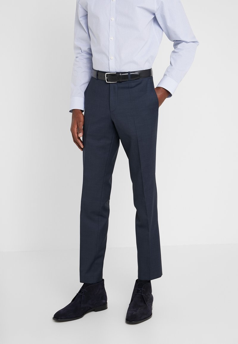 Navy-blau maßgeschneiderte Anzughosen mit glatter Textur, im Slim-Fit-Schnitt, mit gebügelten Falten und einem schwarzen Ledergürtel. Getragen mit dunklen Wildleder-Stiefeletten.