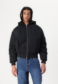 Black puffer jacket with a hood, featuring a zip closure, ribbed cuffs, and side pockets. Smooth fabric with a quilted texture.