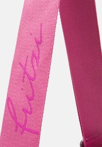 Różowy pleciony pasek z wyhaftowanym logo w ciemniejszym odcieniu różu. Tekstura jest gładka z lekko szorstkim splotem.