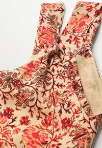 Robe à motifs floraux en beige, avec des motifs rouges et oranges. Comprend des bretelles nouées et une finition texturée pour un aspect doux.