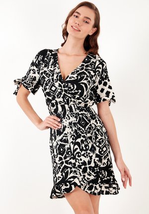 Black and white patterned dress with a V-neck, short sleeves, tie details, and a flared hem. Made from a lightweight, textured fabric.