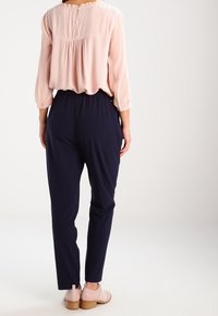 Ljusrosa blus med plisserad rygg, matchad med marinfärgade byxor. Blusen har en rund halsringning och knappar på baksidan.