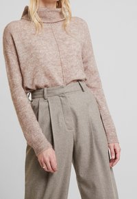 Vaaleanpunainen, struktuuriltaan neuleinen poolopaita, joka on yhdistetty korkeavyötäröisiin, beigeihin housuihin, joissa on laskokset ja sivutaskut.