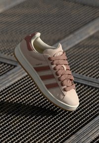 Beige and dusty pink Adidas Campus sneaker with thick laces on a metal grid surface.