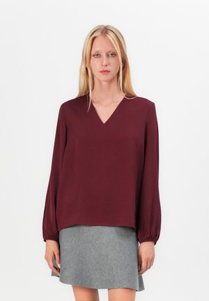 Burgunderfarget V-hals-bluse med lange ermer som er samlet ved håndleddene, kombinert med et grått stoffskjørt, med glatt tekstur og enkelt design.