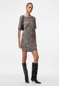 Īsām piedurkņu pieguļošs kleita, kas pārklāta ar sekvīnēm, sudraba un bronzas toņos, kombinēta ar ceļgala augstiem, spīdīgiem melniem zābakiem un nelielu melnu somiņu.