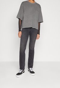 Camiseta gris de gran tamaño con mangas cortas, superpuesta a una camiseta negra de manga larga. Combinada con jeans negros y zapatillas negras y blancas.