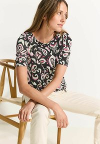 Camiseta de manga corta negra con patrones en espiral coloridos en rosa, blanco y verde. Tejido suave, escote redondo y corte relajado.