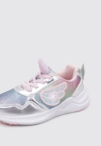 Zapatilla deportiva plateada con paneles degradados iridiscentes, acentos en rosa y detalles en forma de alas. Presenta un material suave y una suela de goma.