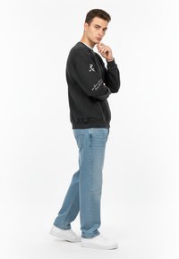 Felpa nera con scollo a girocollo, dettaglio in testo bianco sulla manica, abbinata a jeans a gamba dritta blu chiaro e sneakers bianche.