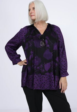 Purple blouse with floral and polka dot patterns, long sleeves, loose fit, and a v-neckline. Black pants are worn underneath.