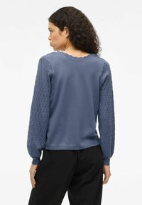 Sudadera azul con mangas de punto texturizado, escote redondo con borde ondulado y corte relajado. Tejido suave en el cuerpo y detalles sutiles en las mangas.