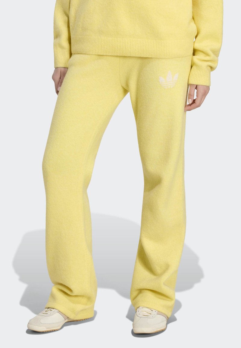 Personne portant un pantalon de jogging jaune ample avec un léger logo sur la cuisse gauche et un pull jaune assorti, associé à des baskets blanches.
