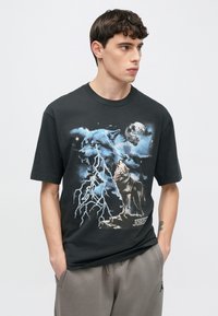 Schwarzes Baumwoll-T-Shirt mit einem grafischen Design von zwei Wölfen vor einem blau-grauen Nachthimmel, mit Blitz und Mond. Lässige Passform.